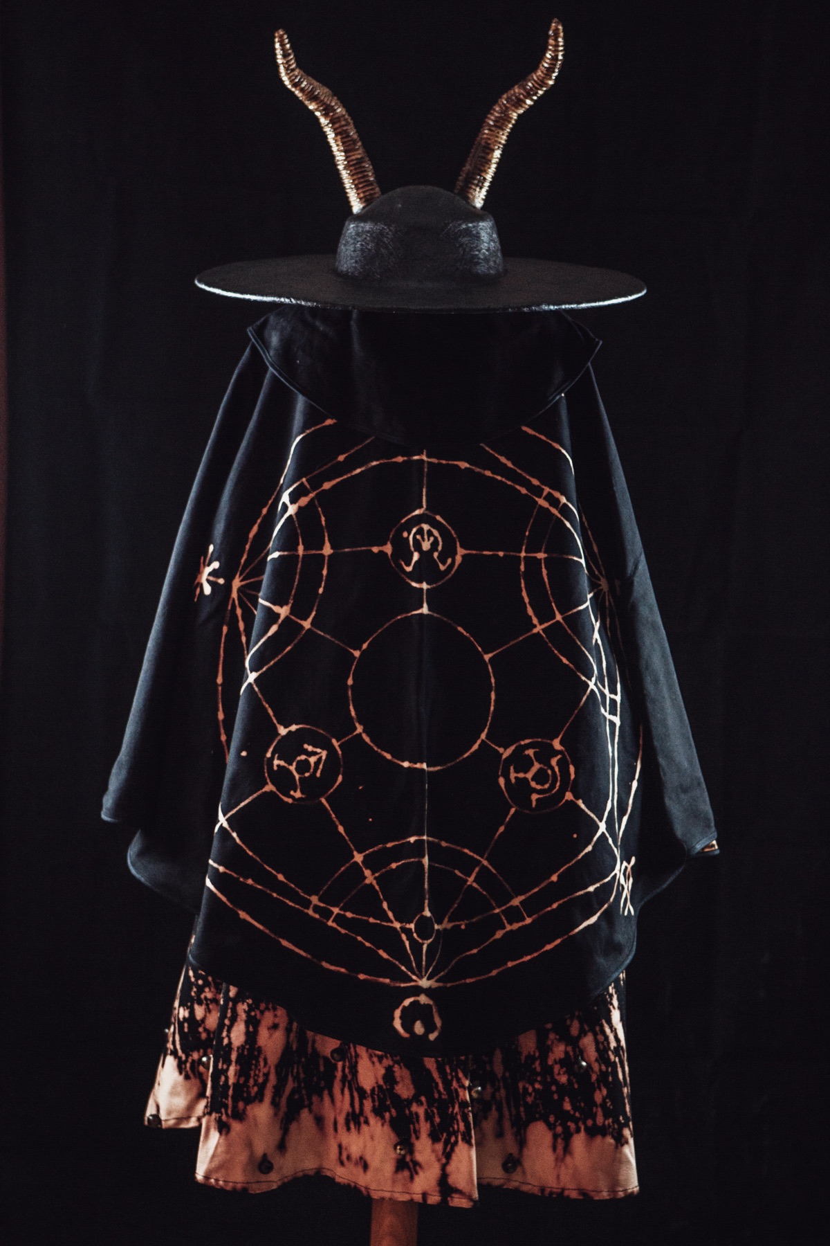 La Diablessa d'esquena: el barret amb banyes i la capa amb el cercle de sigils pintat a mà